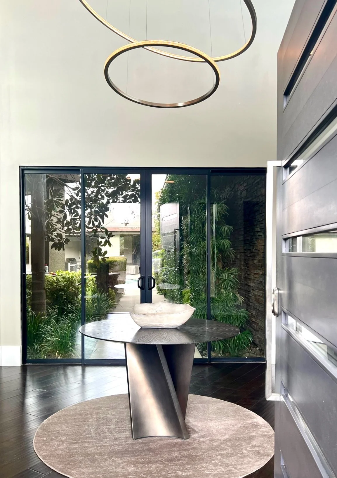 Dragon Residence entry — twisted steel pedestal table under ring chandeliers, glass walls to the courtyard