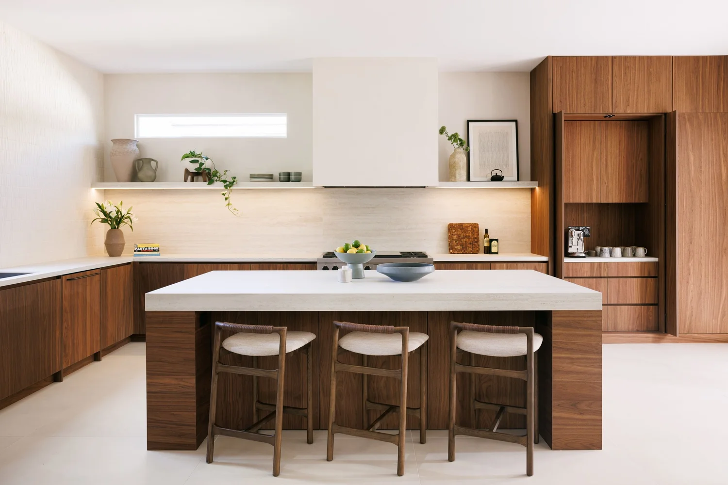 Farr Residence kitchen — walnut cabinetry, pale stone waterfall island, and woven counter stools
