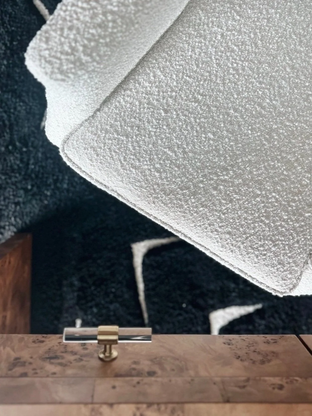 Detail from a MIC & NAY interior — boucl&eacute; chair over a black patterned rug beside a burl wood table