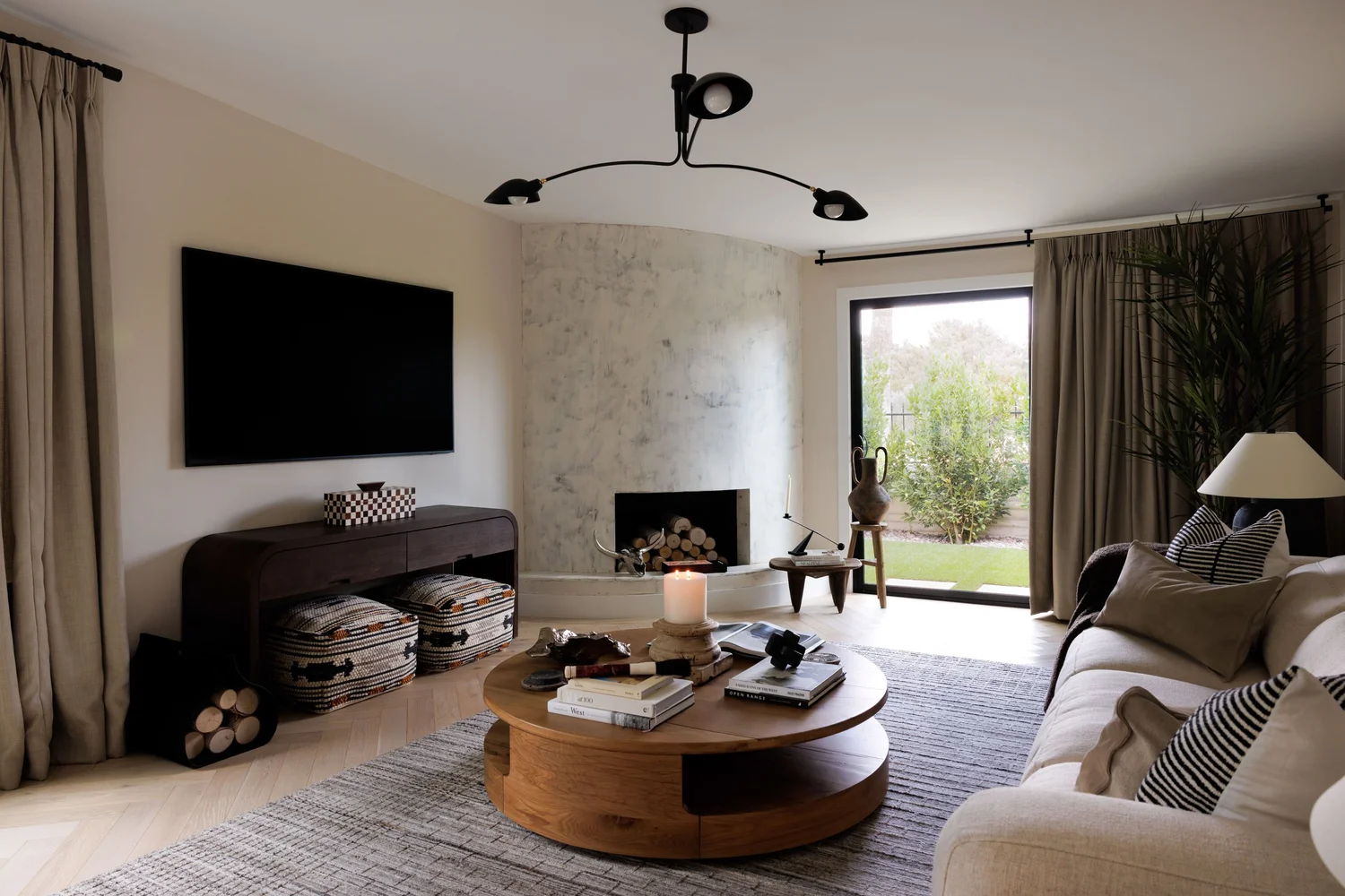 Spanish Oaks Residence living room by MIC & NAY — plaster fireplace, round oak coffee table, and linen drapery