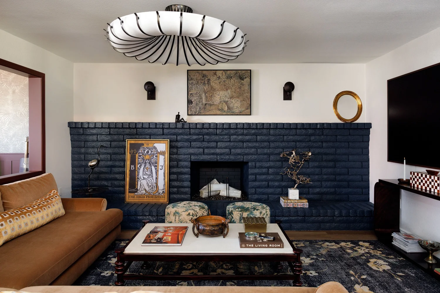 Storrie Residence living room — navy painted brick fireplace, camel sofa, and vintage art